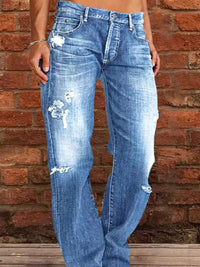 Blue distressed jeans worn by a person against a brick wall.