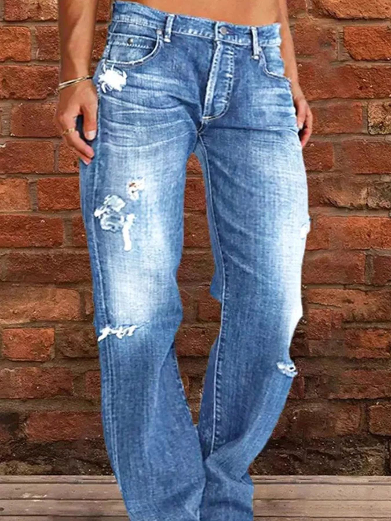 Blue distressed jeans worn by a person against a brick wall.