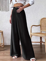 Person wearing black wide-leg pants and a white top in a room with a textured wall and wooden floor.