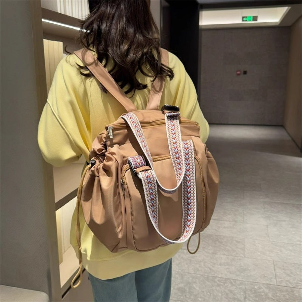 Person holding a large brown backpack with decorative straps in an indoor setting