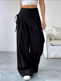Person wearing black wide-leg pants with a white top in a minimalistic room.