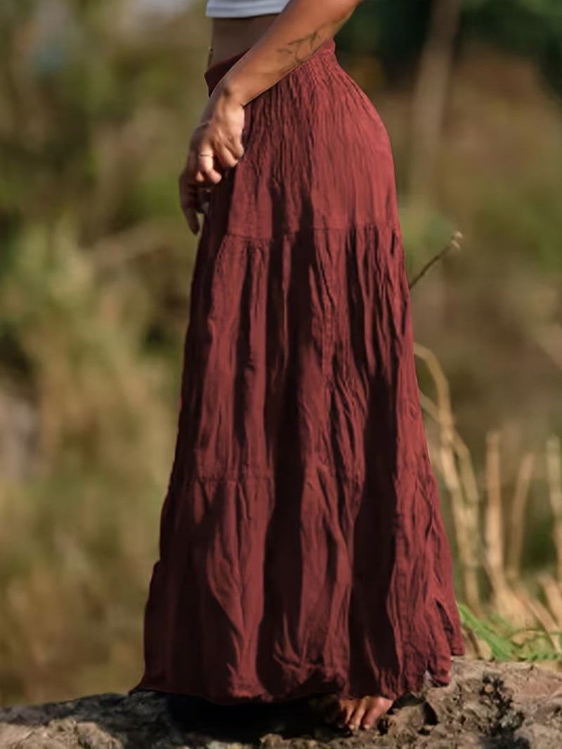 Person wearing a long burgundy skirt standing outdoors with a blurred natural background