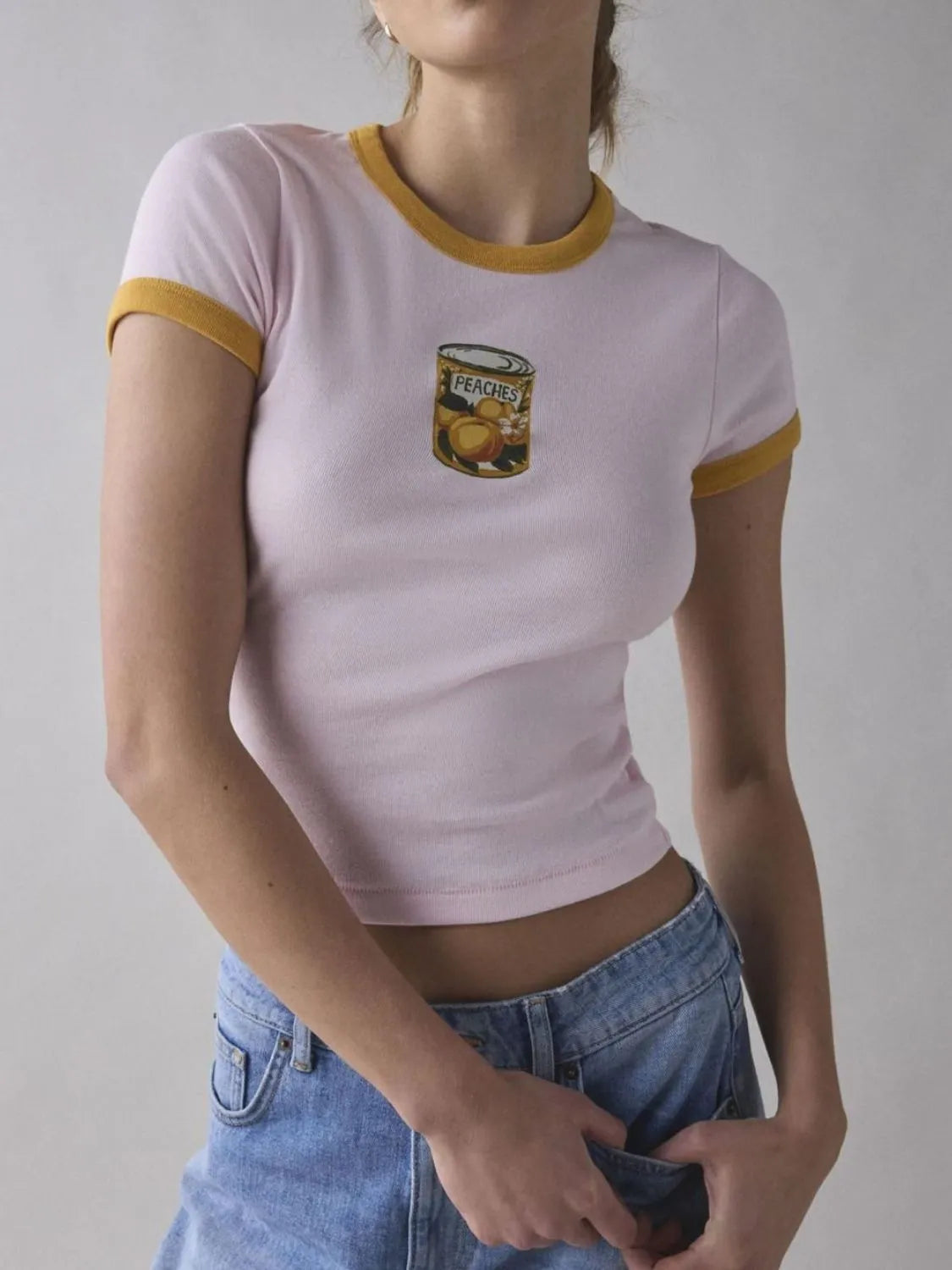 Person wearing a pink t-shirt with a graphic design on a plain background