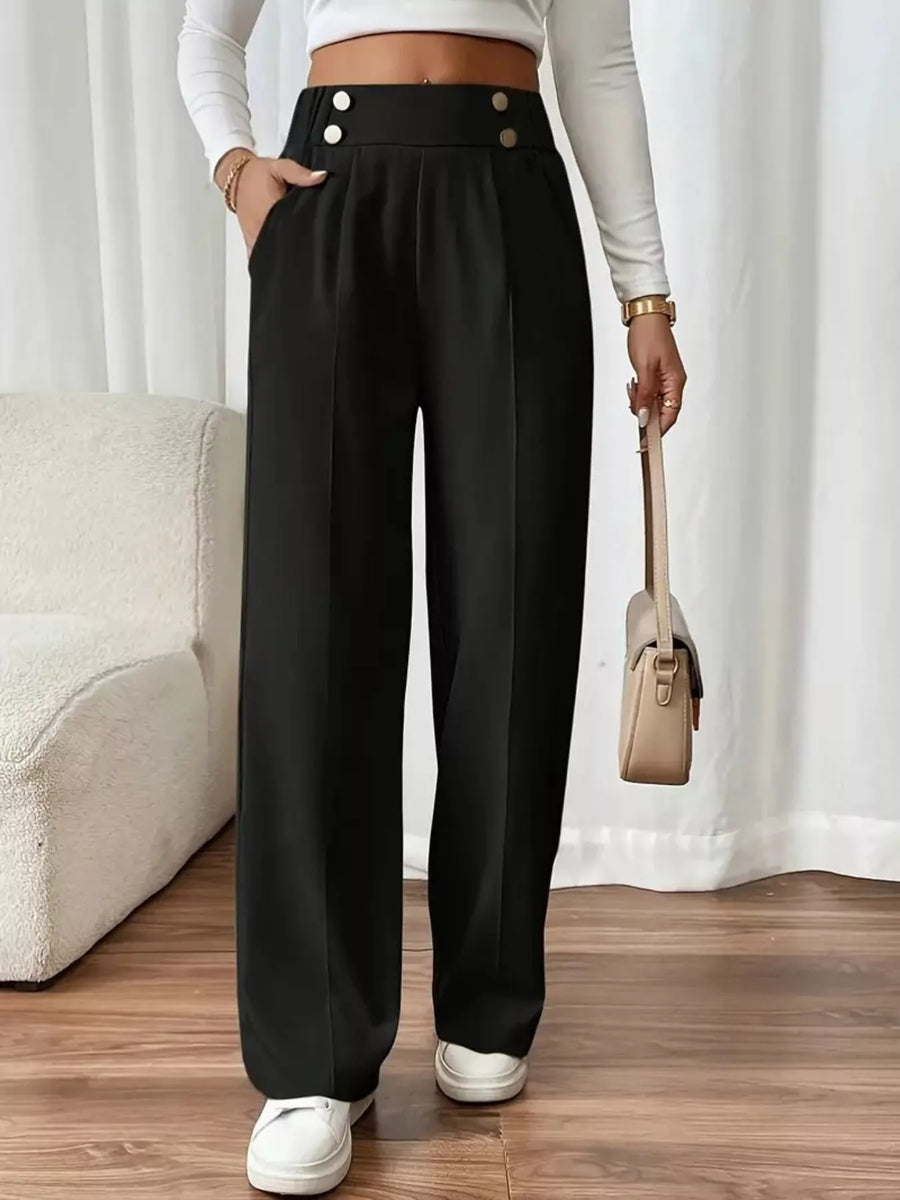 Person wearing black high-waisted pants with white buttons, standing indoors.