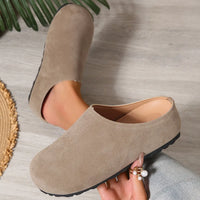 Beige clogs worn by a person on a neutral background