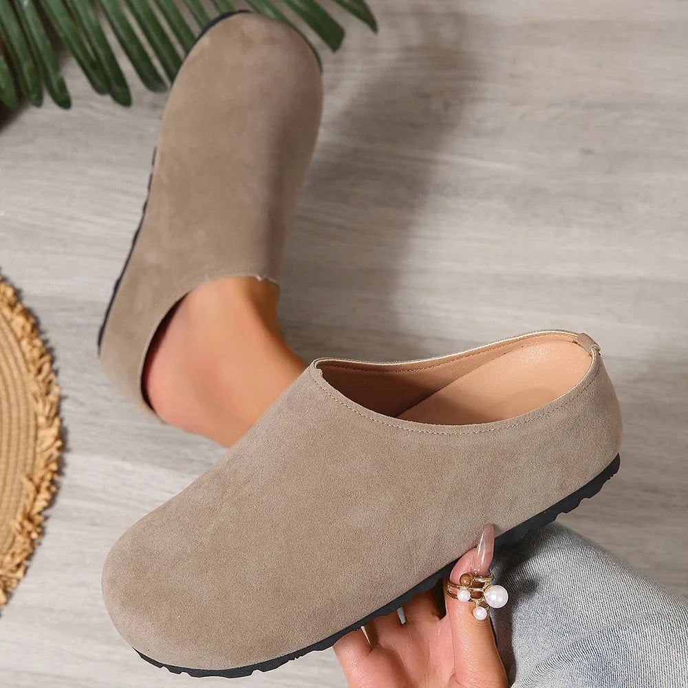 Beige clogs worn by a person on a neutral background