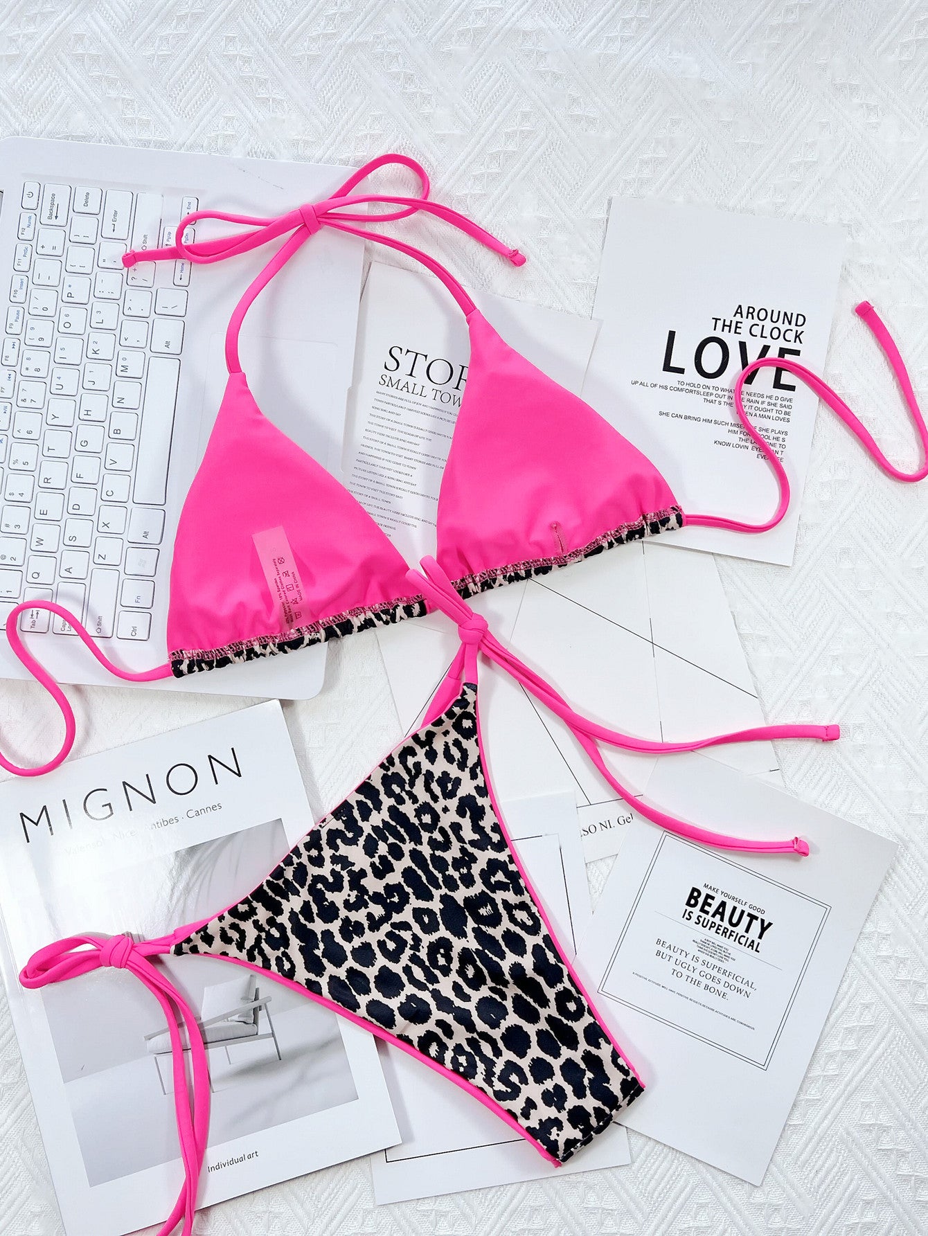 Pink bikini with leopard print bottom on a white surface with magazines underneath