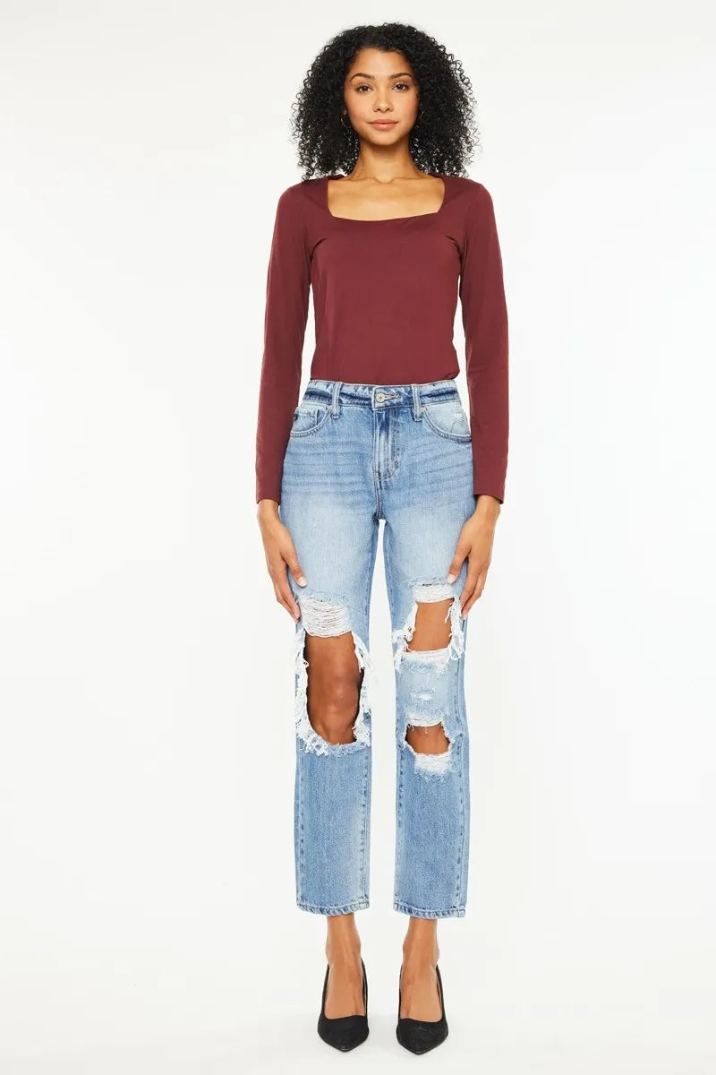 Woman wearing a burgundy long-sleeve top and light blue ripped jeans on a white background