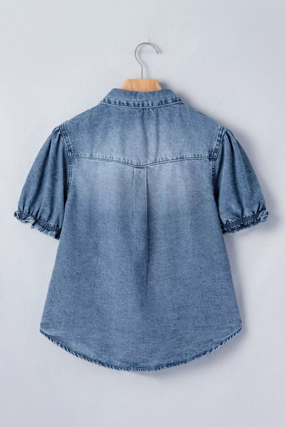 Blue denim shirt with puff sleeves on a hanger against a light gray background