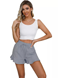 Woman wearing a white sleeveless top and gray shorts on a white background