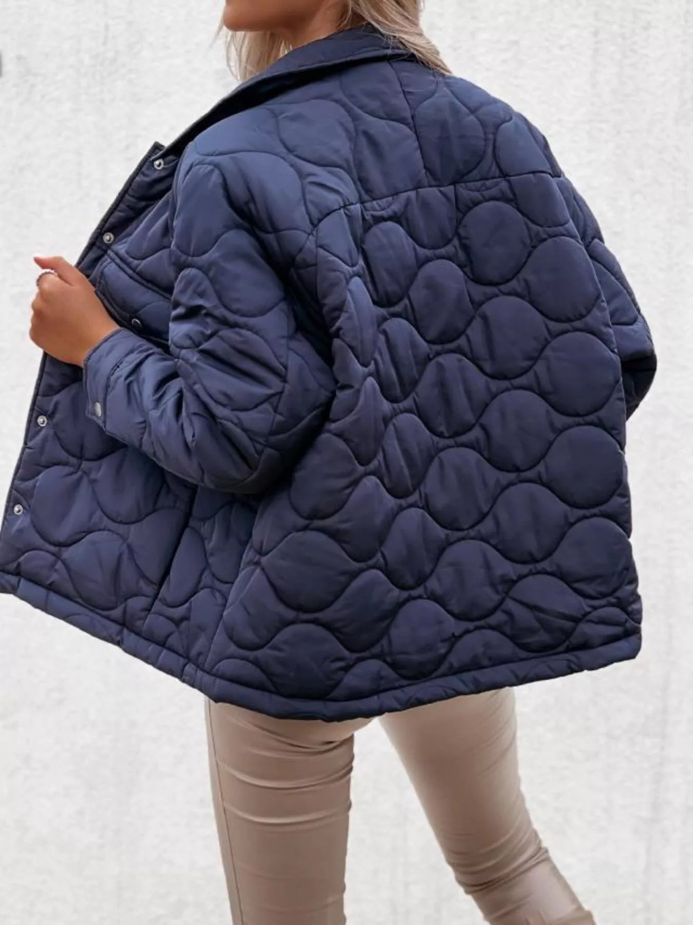Navy quilted jacket worn by a person on a light gray background
