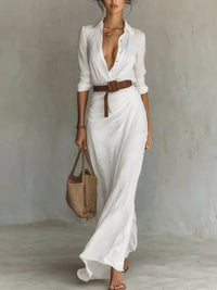 Woman wearing a white dress with a brown belt and holding a straw bag against a plain background