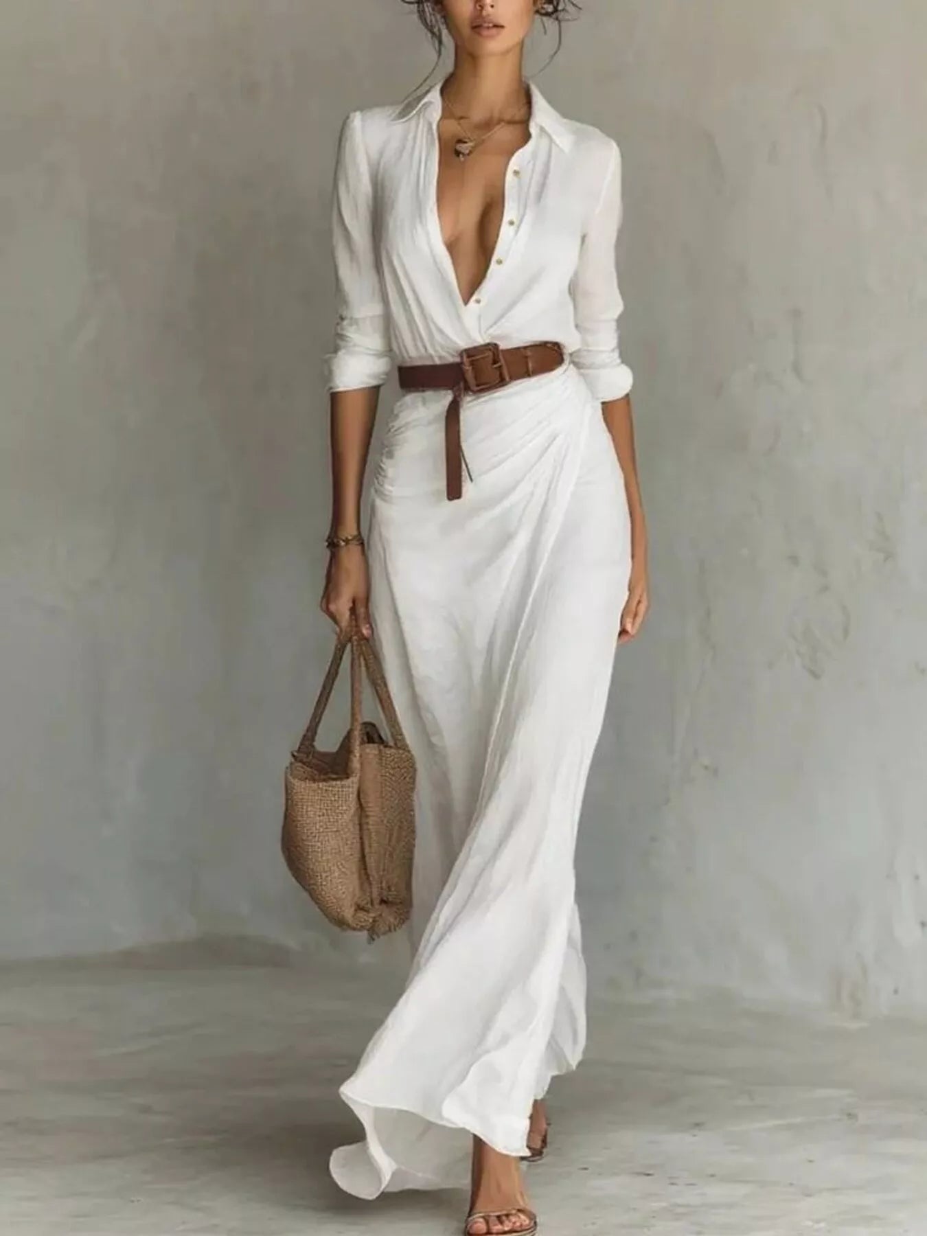 Woman wearing a white dress with a brown belt and holding a straw bag against a plain background