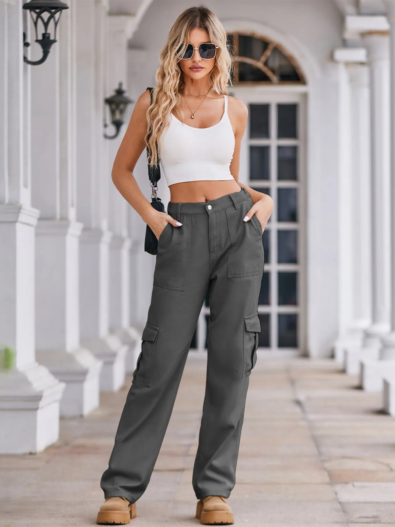 Woman wearing a white crop top and gray cargo pants standing on a porch.
