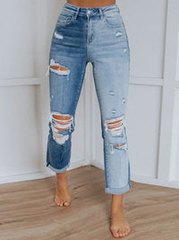 Ripped blue jeans worn by a person against a white wall.