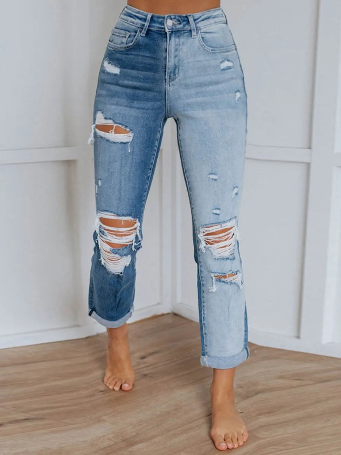 Ripped blue jeans worn by a person against a white wall.