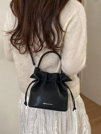 Black handbag with drawstring held by a person wearing a white outfit.