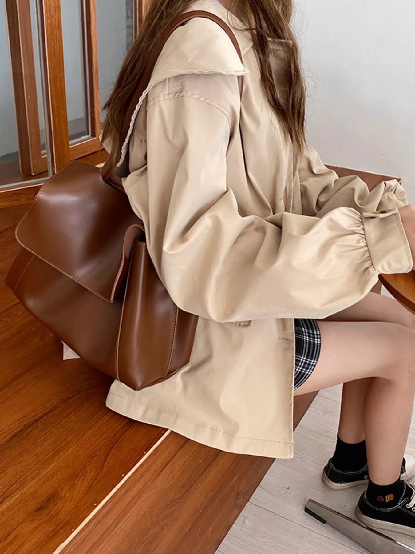Person wearing a beige jacket holding a brown leather bag indoors.