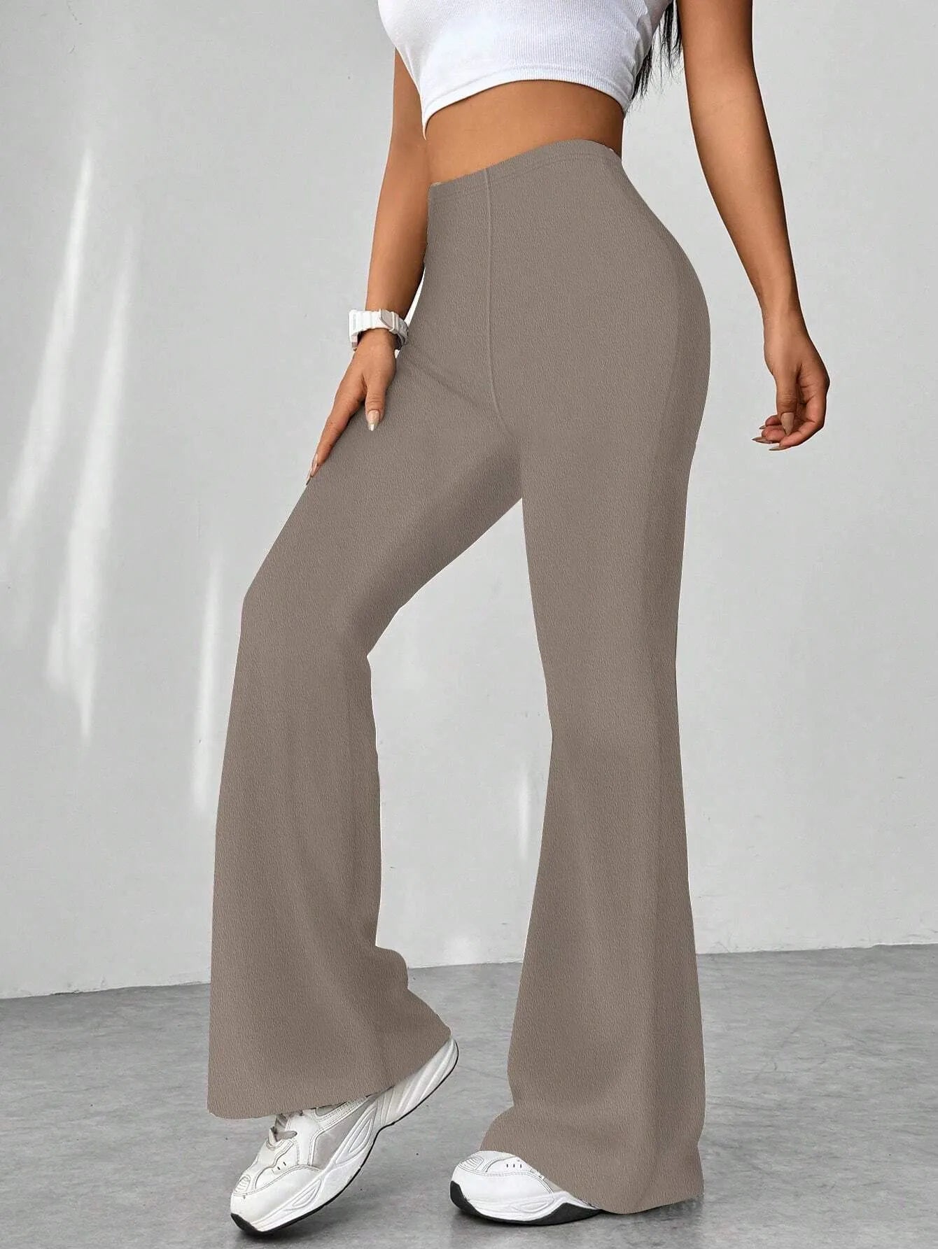 Person wearing brown wide-leg pants with a white top and sneakers on a plain background