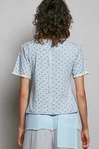Person wearing a light blue patterned shirt with white trim on a plain background