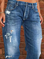 Blue jeans with distressing details worn by a person against a brick wall.