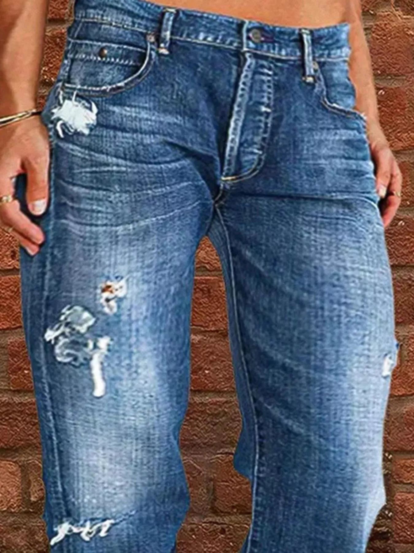 Blue jeans with distressing details worn by a person against a brick wall.