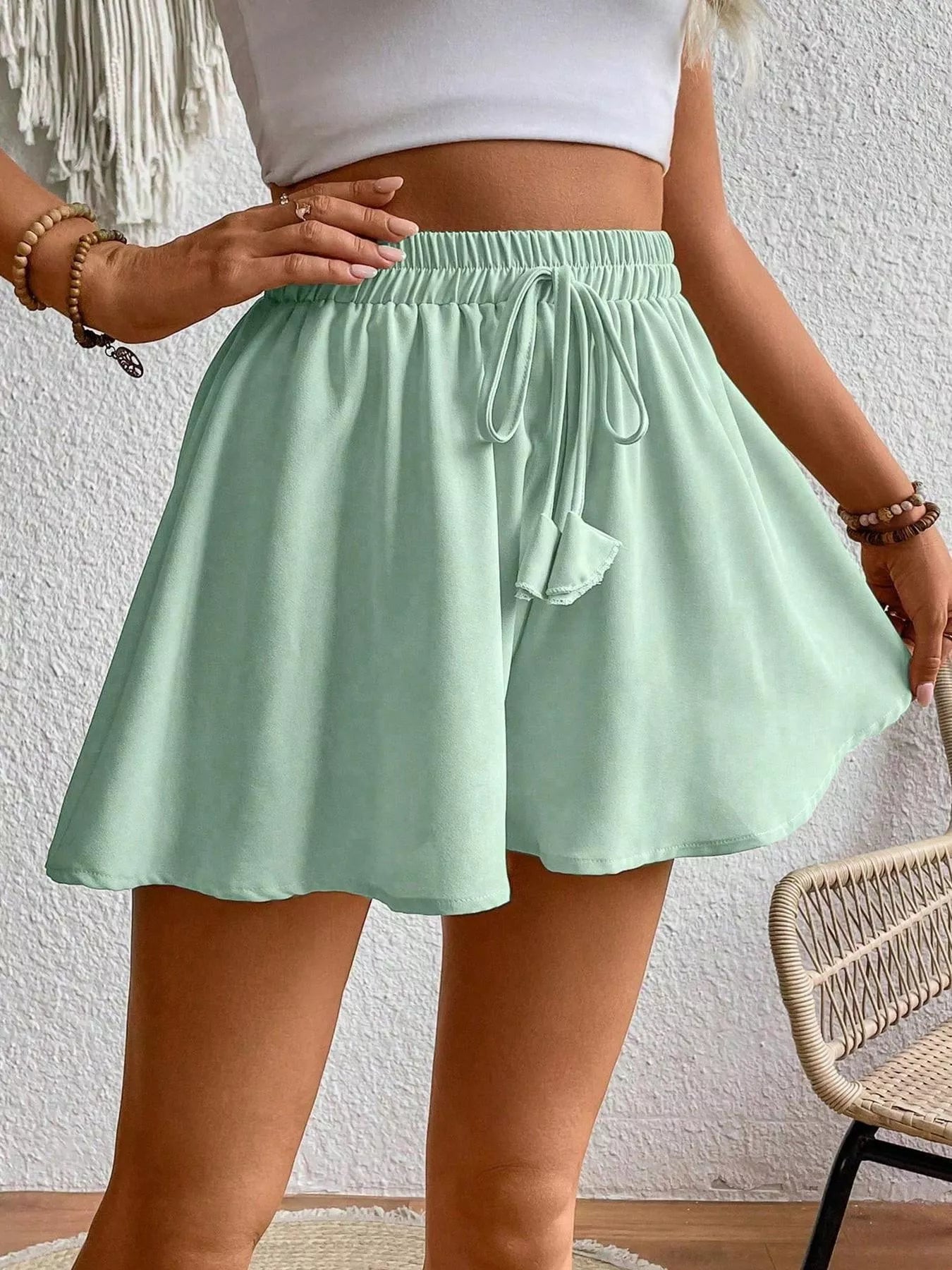 Person wearing a light green skirt with a white top against a textured wall.