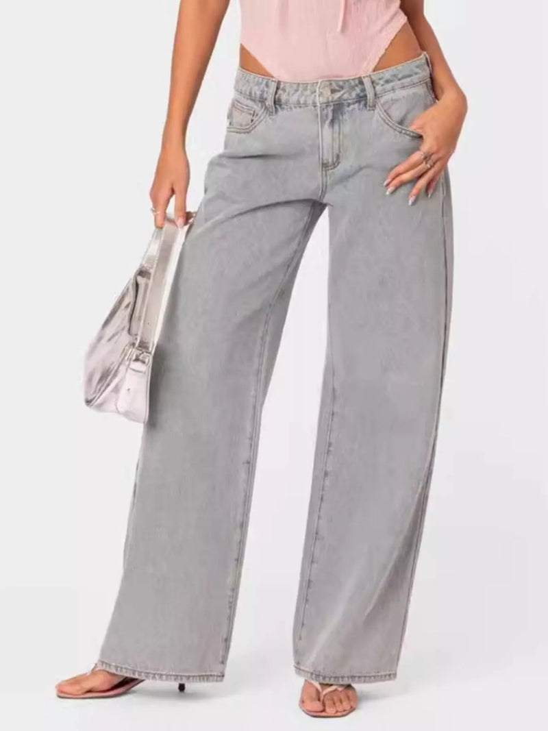 Person wearing light gray wide-leg jeans and a pink top, holding a clear handbag on a white background.