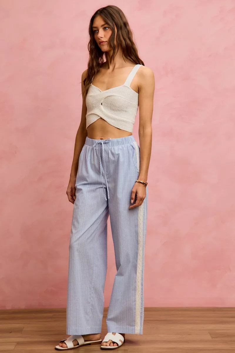 Woman wearing a light-colored top and blue checkered pants against a pink wall.