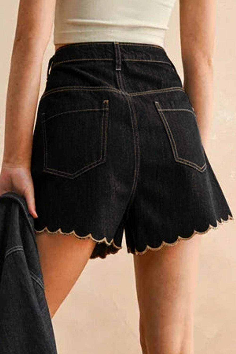 Black denim skirt with scalloped hem worn by a person on a beige background