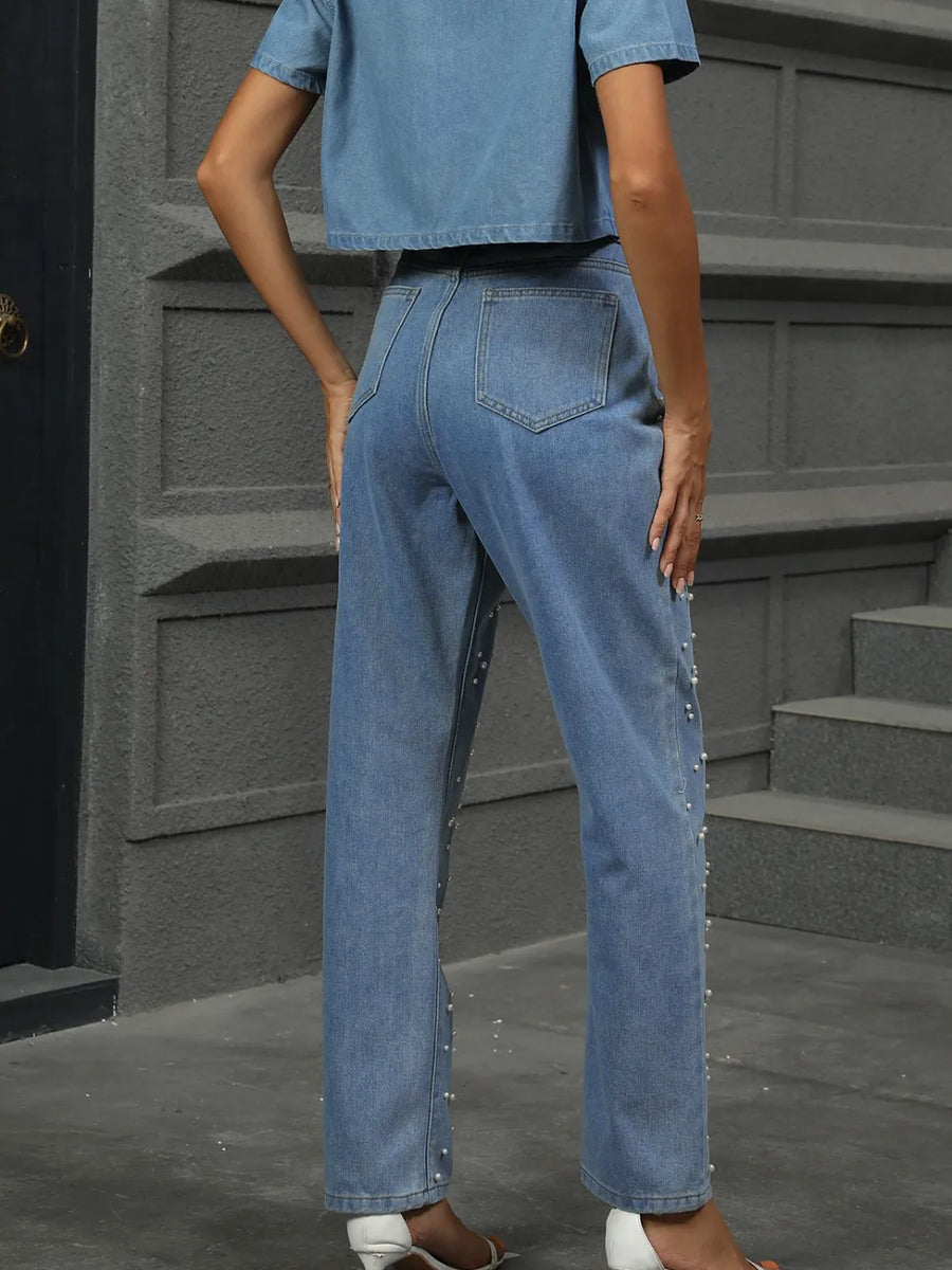 Person wearing blue jeans standing on a gray pavement with a gray wall in the background