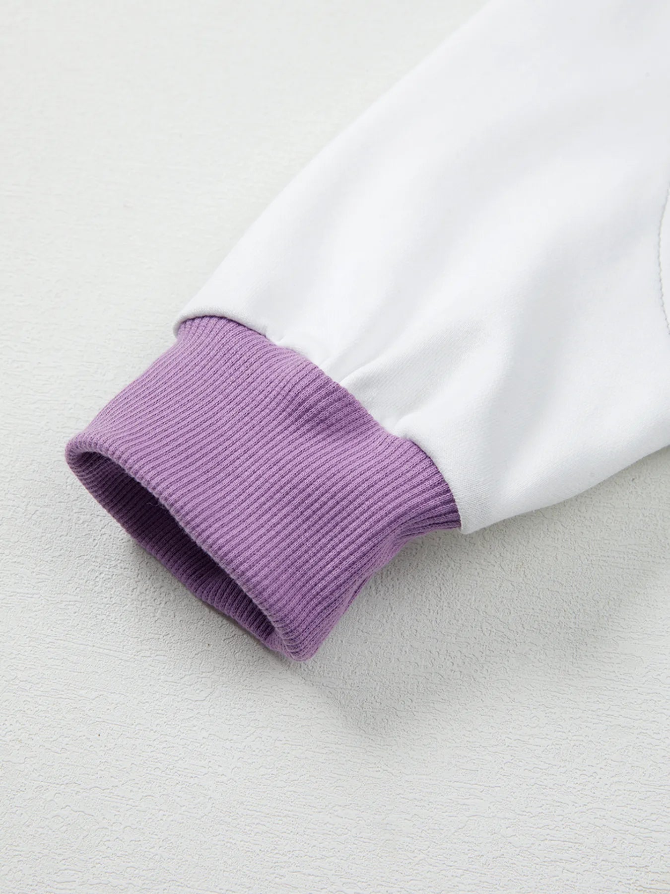 Close-up of a white garment with purple ribbed cuffs on a light gray background
