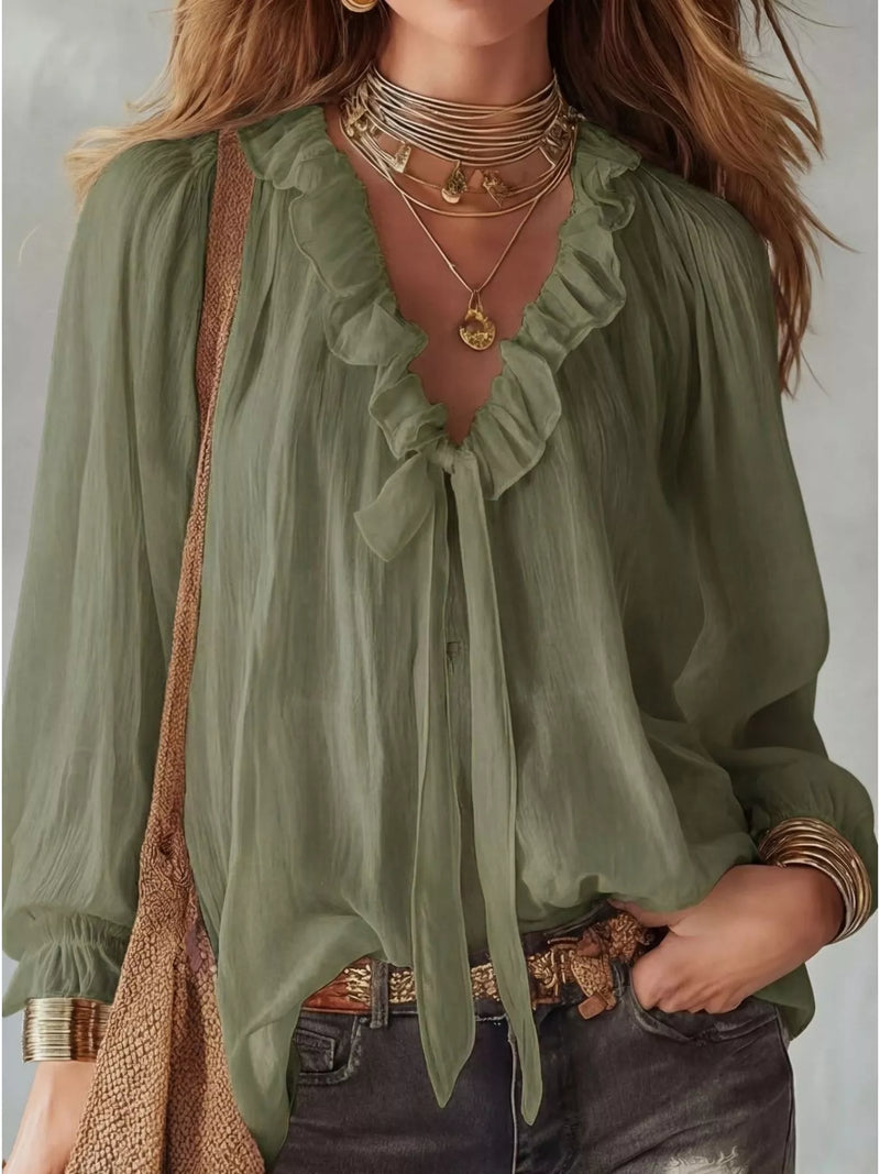 Woman wearing a green blouse with ruffled details and layered necklaces against a neutral background