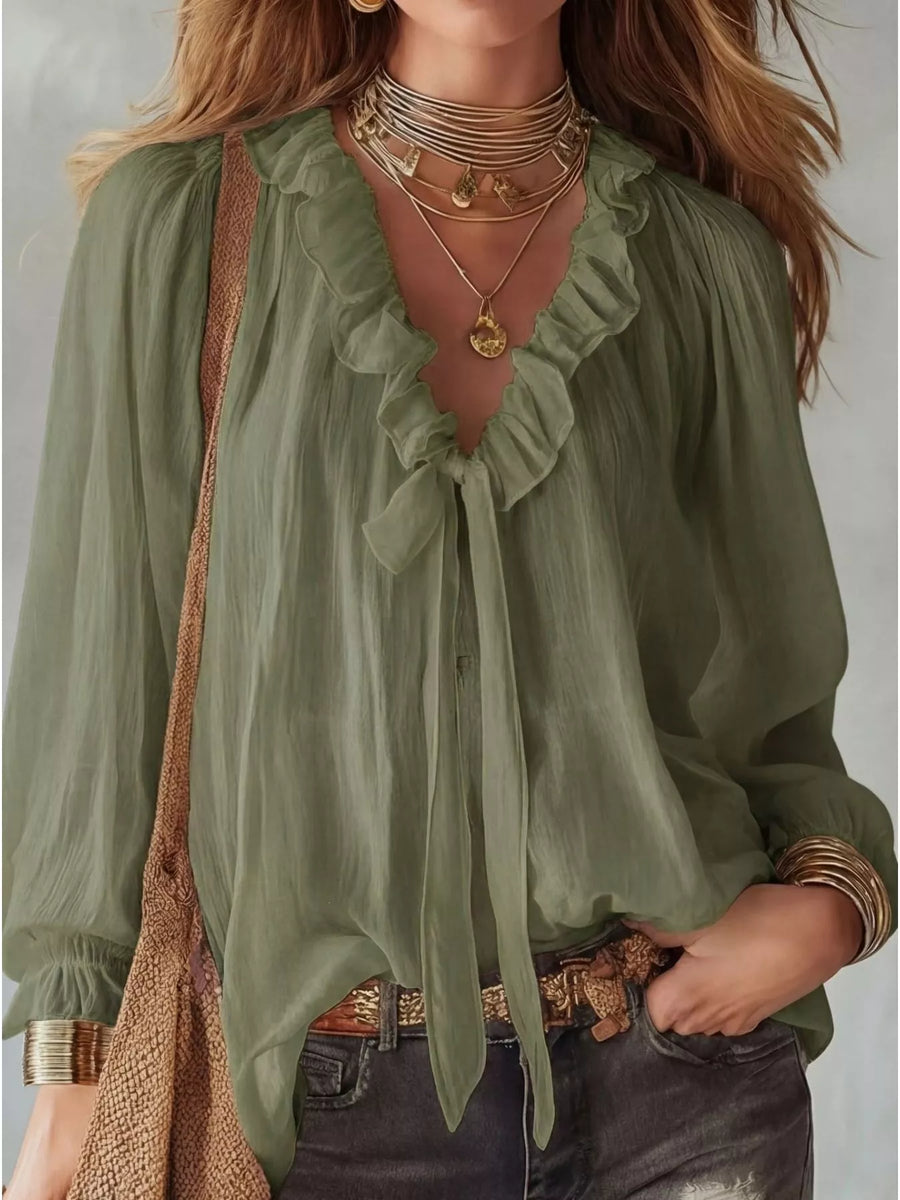 Woman wearing a green blouse with ruffled details and layered necklaces against a neutral background