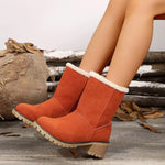 Orange suede boots with white fur lining worn by a person, with a rustic background.