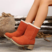 Orange suede boots with white fur lining worn by a person, with a rustic background.