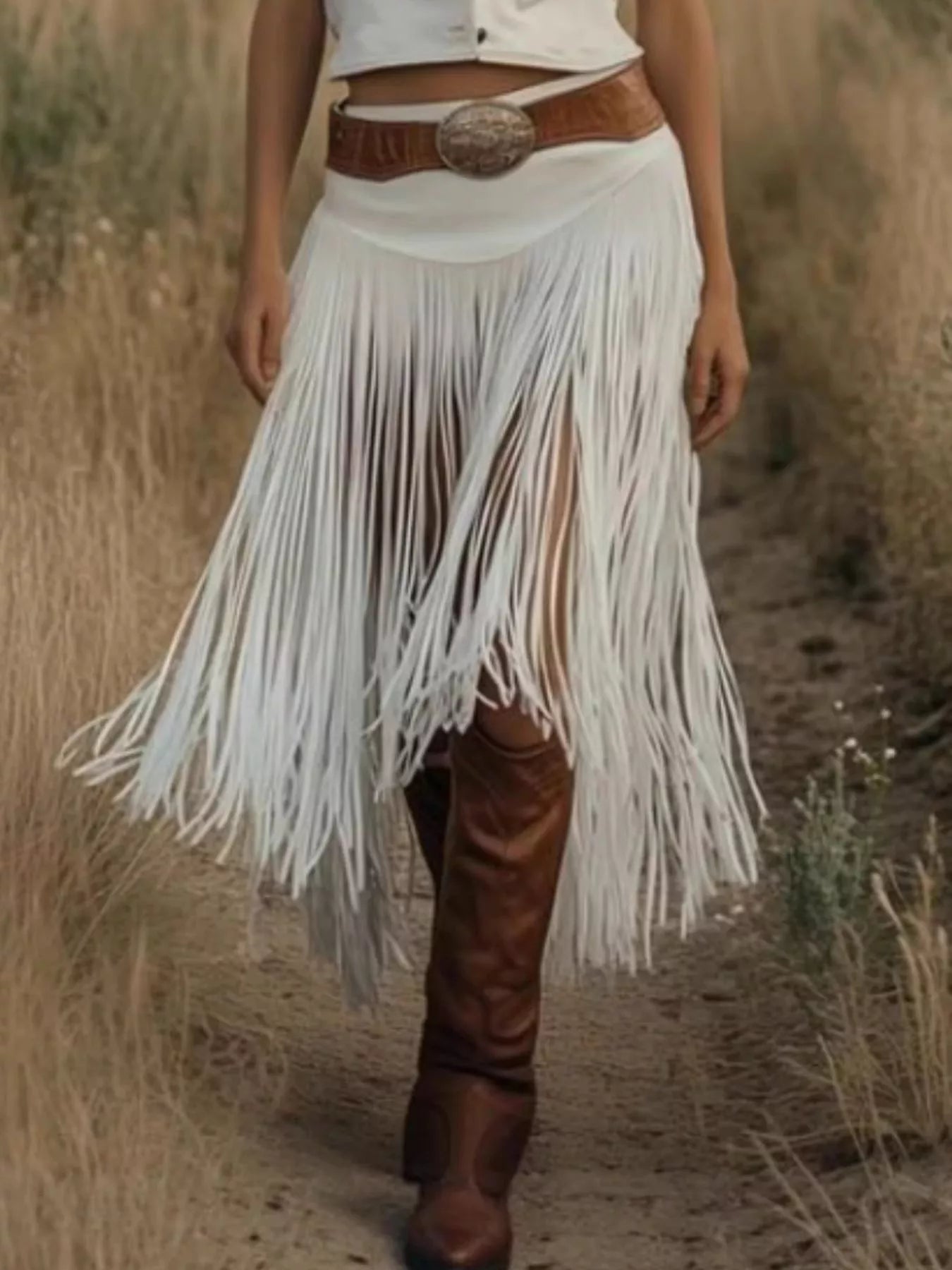 Person wearing a white fringe skirt with brown boots and belt in a natural setting