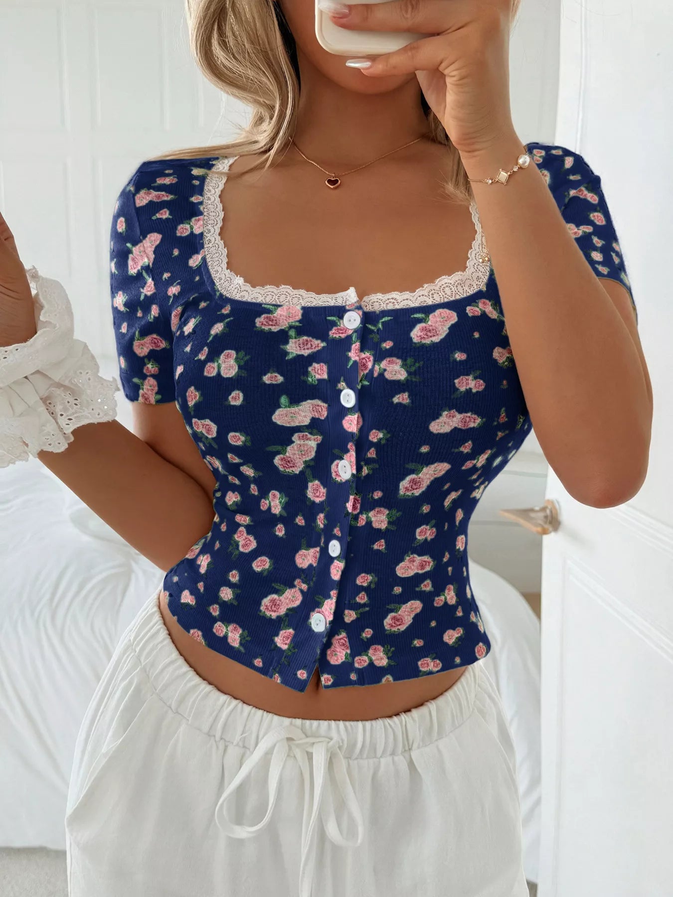 Woman wearing a blue floral pajama top with white pants in a bedroom setting.
