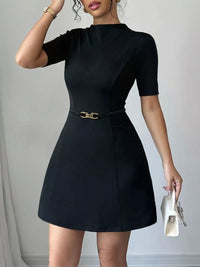 Woman wearing a black dress with a gold belt against a gray background