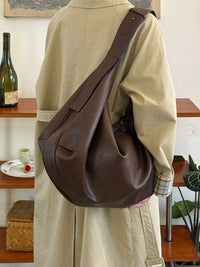 Person wearing a brown leather shoulder bag in an indoor setting