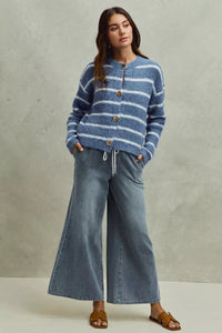 Woman wearing a blue striped sweater and wide-leg jeans against a neutral background
