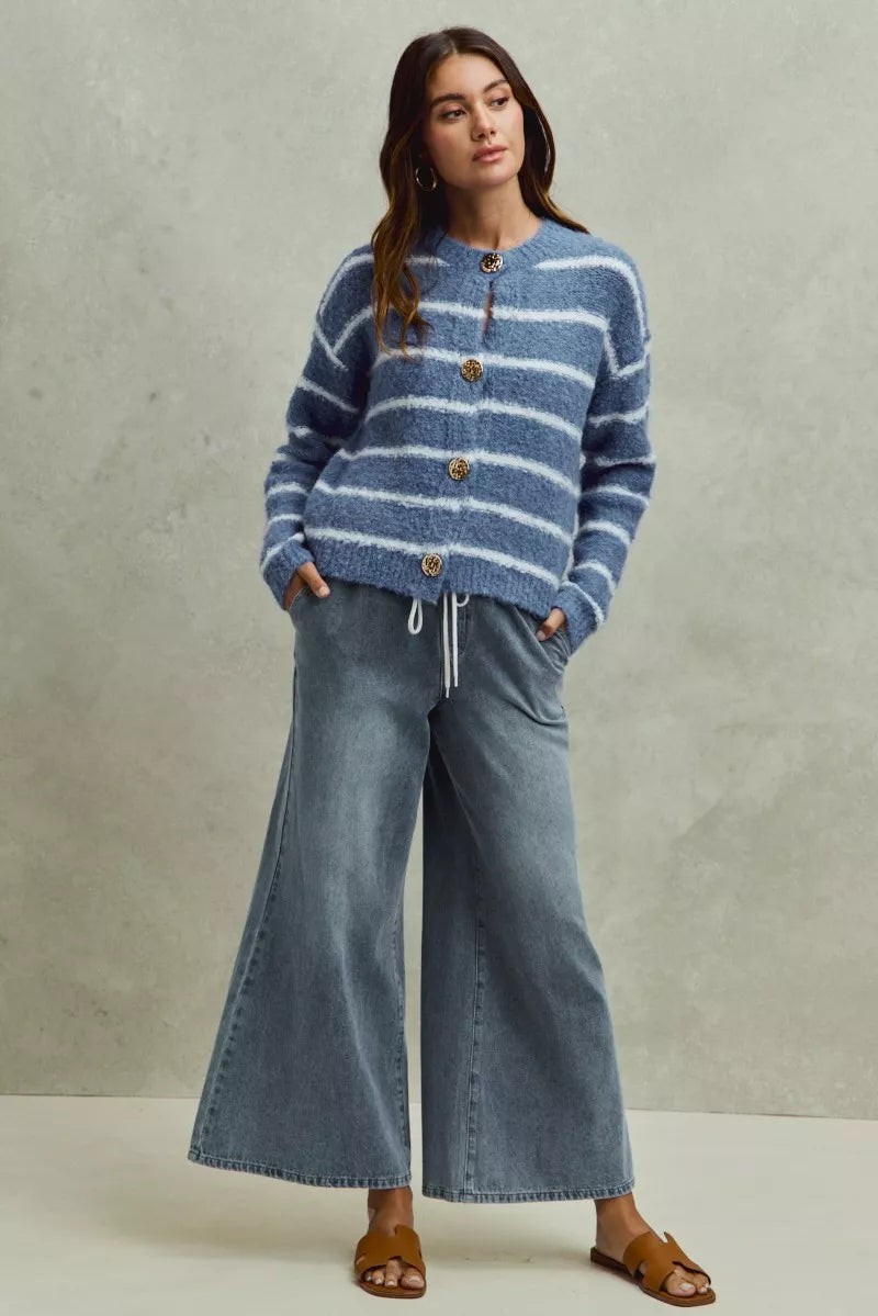 Woman wearing a blue striped sweater and wide-leg jeans against a neutral background