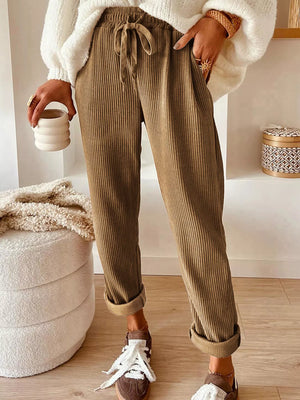Person wearing brown ribbed pants with a white fluffy sweater and white sneakers, holding a ceramic cup.