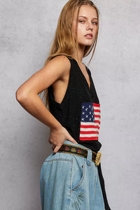 Person wearing a black tank top with an American flag design and blue jeans against a gray background