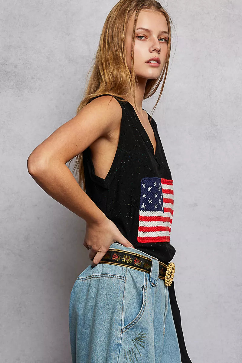 Person wearing a black tank top with an American flag design and blue jeans against a gray background
