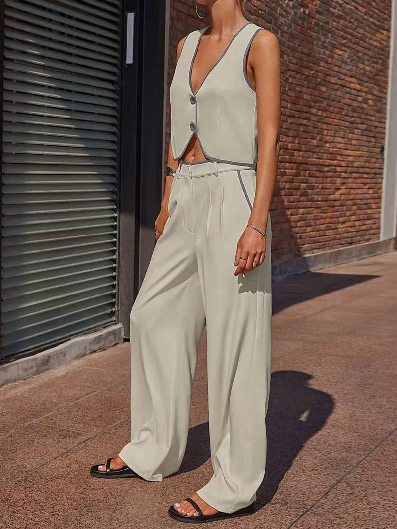 Person wearing a light gray sleeveless top and wide-leg pants standing against a brick wall.