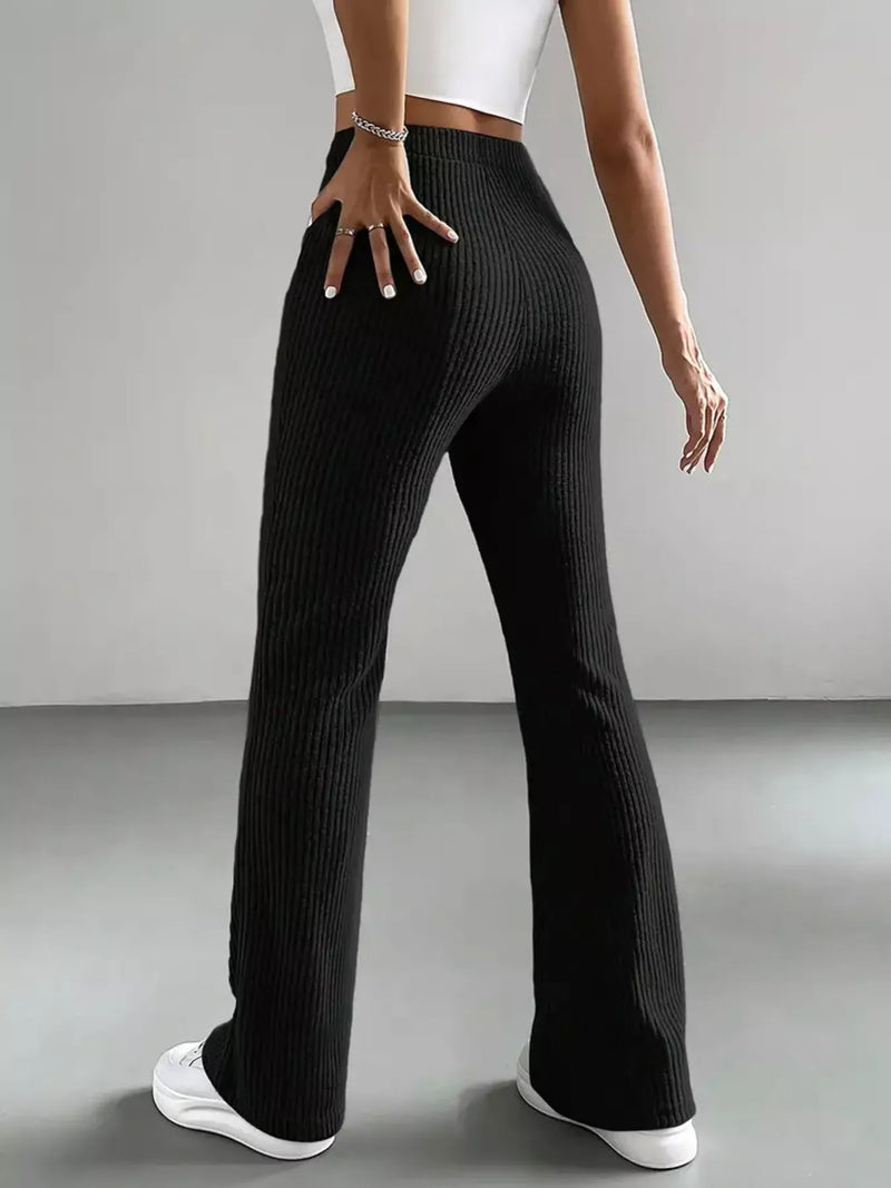 Person wearing black ribbed pants and white sneakers on a gray background
