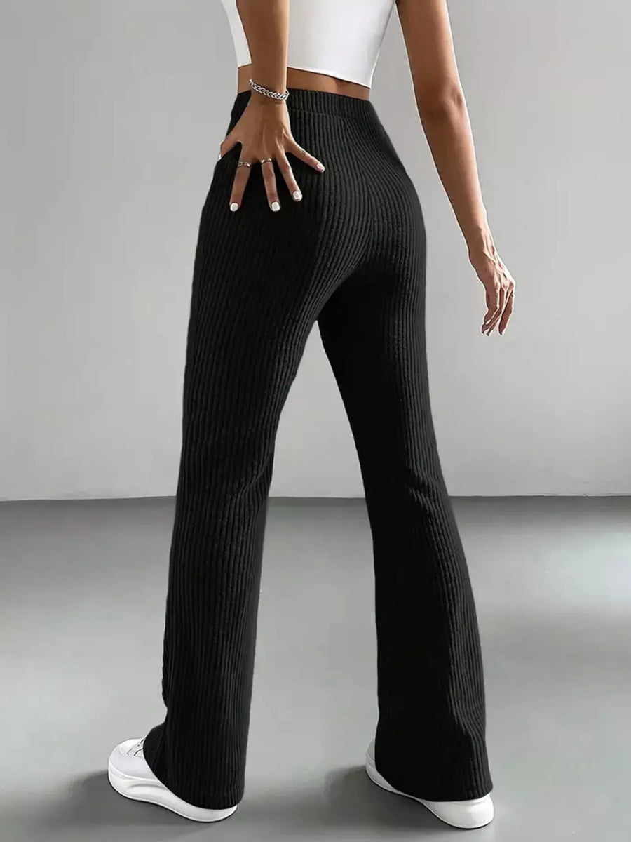 Person wearing black ribbed pants and white sneakers on a gray background
