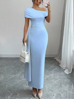 Woman wearing a light blue off-shoulder dress holding a white handbag indoors.