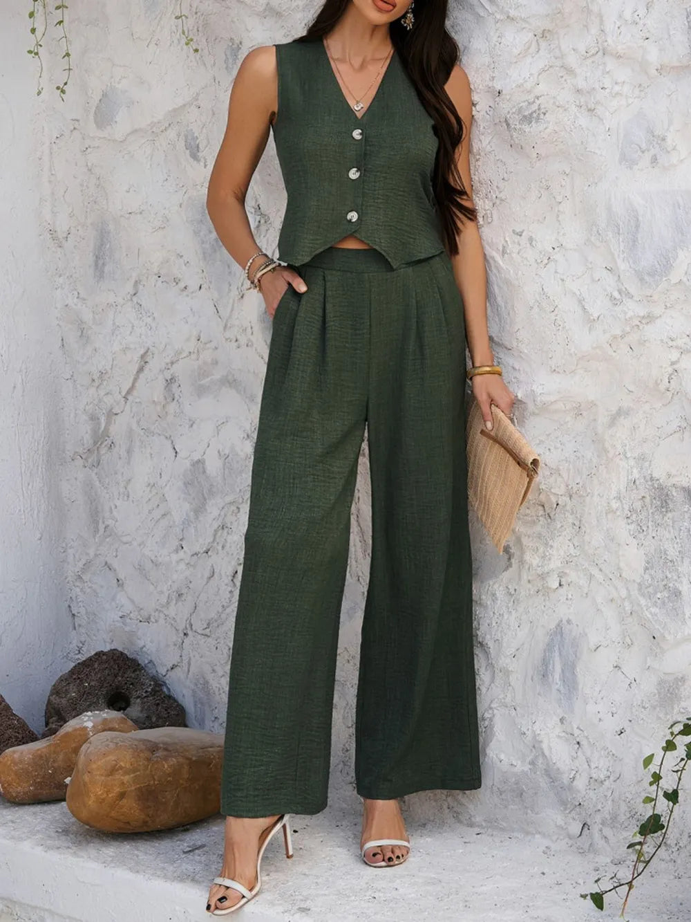 Woman wearing a green outfit with a vest and wide-leg pants against a textured wall.